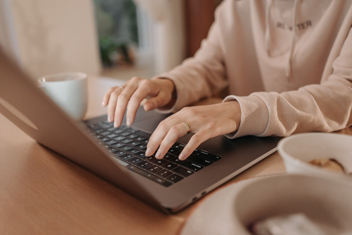 Person typing on a laptop with a cup and plate on a table